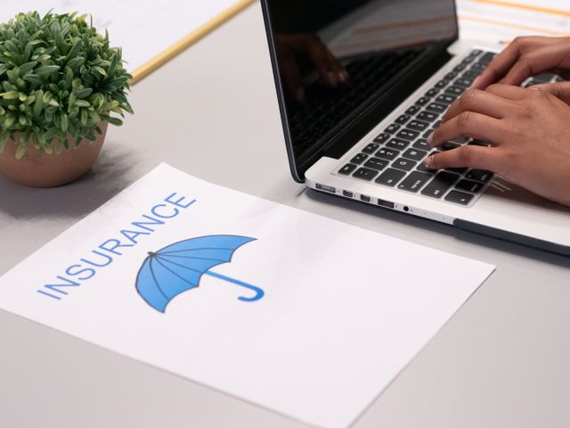 a person using a laptop next to an insurance paper